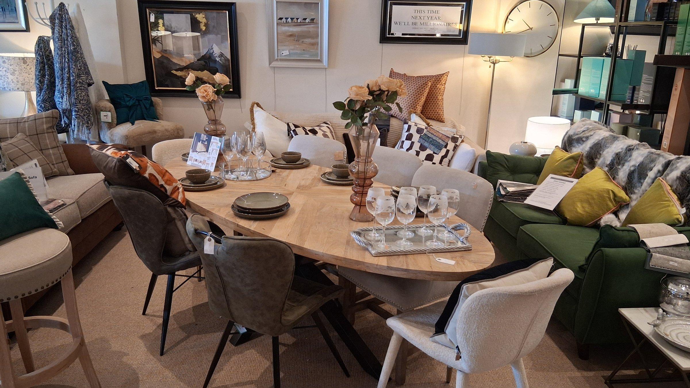 Oval dining table styled with glassware, surrounded by accent chairs and sofas in the Canwell showroom