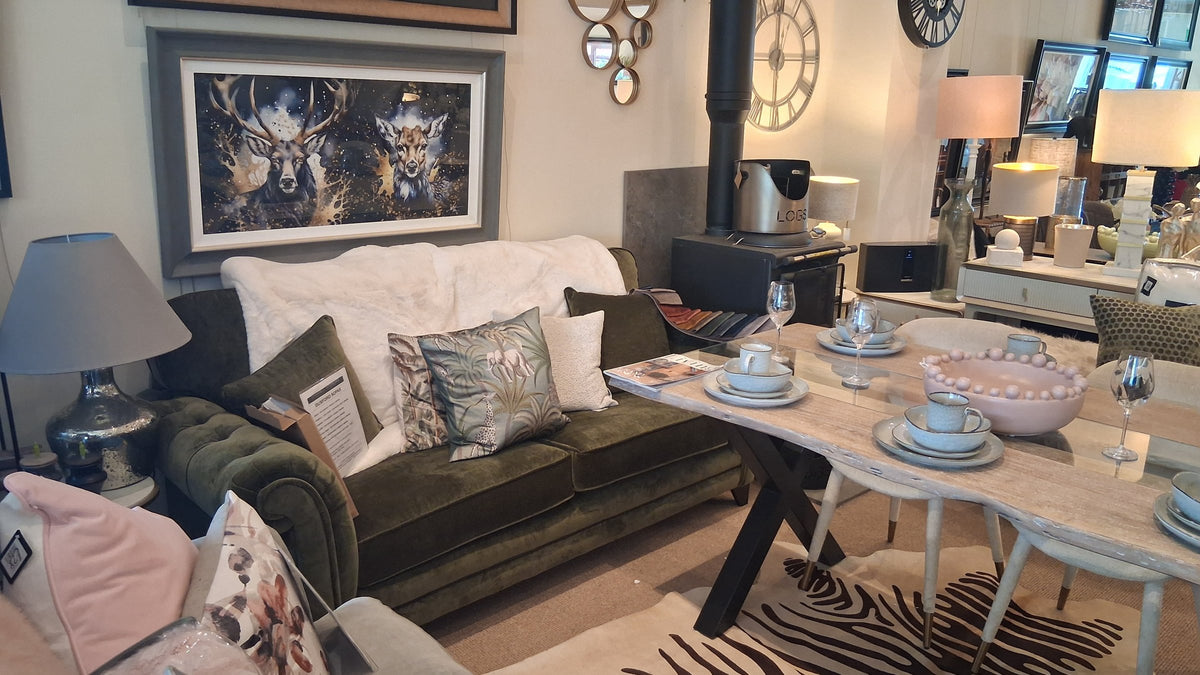 A green velvet sofa with cushions and a throw beside a wood burner and a dining table in the Canwell showroom